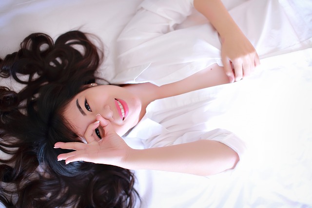 Jeune femme habillée en blanc, allongée sur un lit.