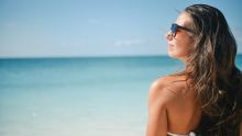 Femme de dos, le visage de profil, sur une plage en été.