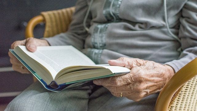 Personne âgée en train de lire un livre en maison de retraite.