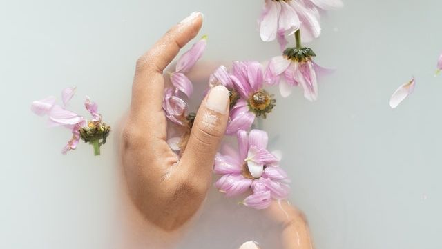 Main baignant dans une eau florale laiteuse avec des fleurs.